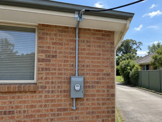 Brick house wall with overhead service cable, point-of-attachment bracket and meter box in Macquarie Hills
