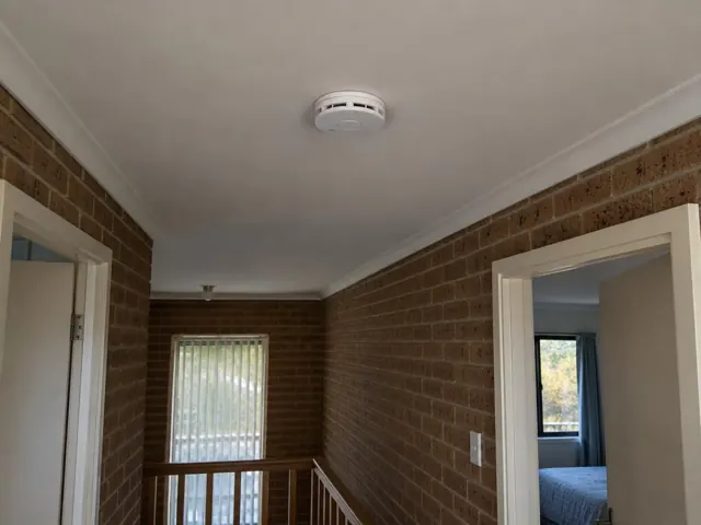 Ceiling smoke alarm in a brick hallway with doorways and stairs in Cardiff Heights